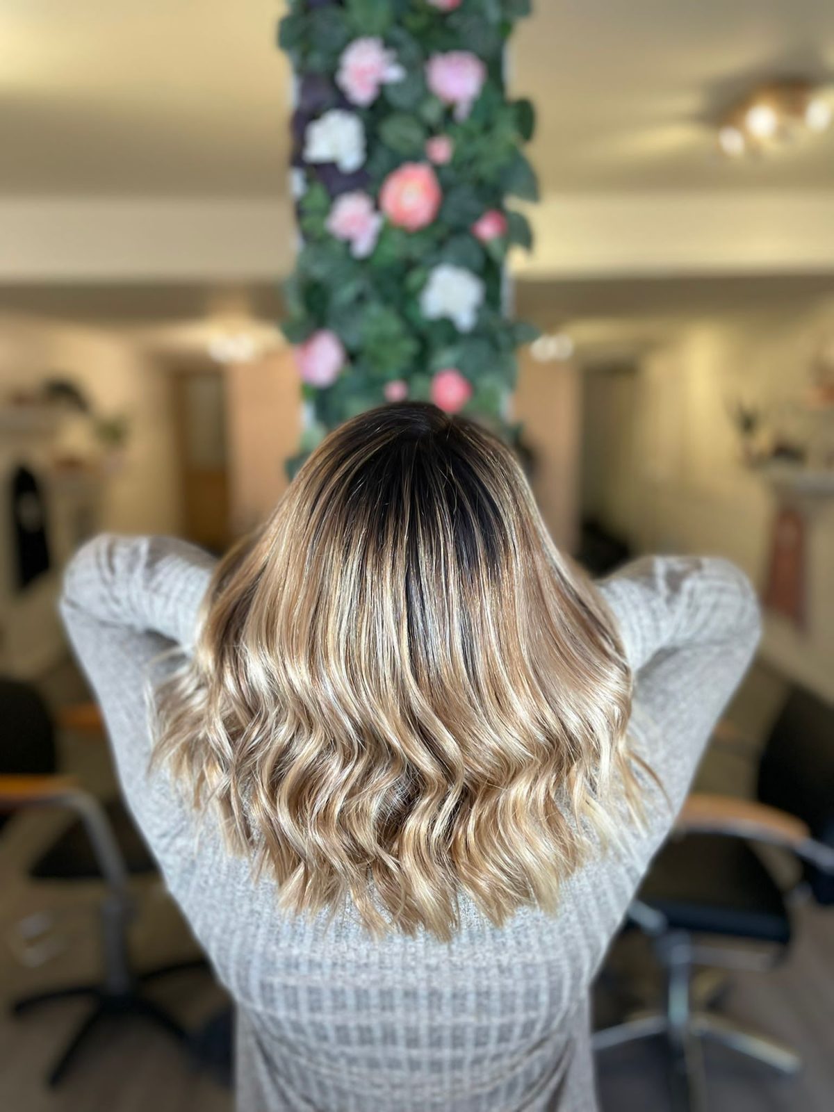 A rooted blonde balayage with soft waves, seen from behind